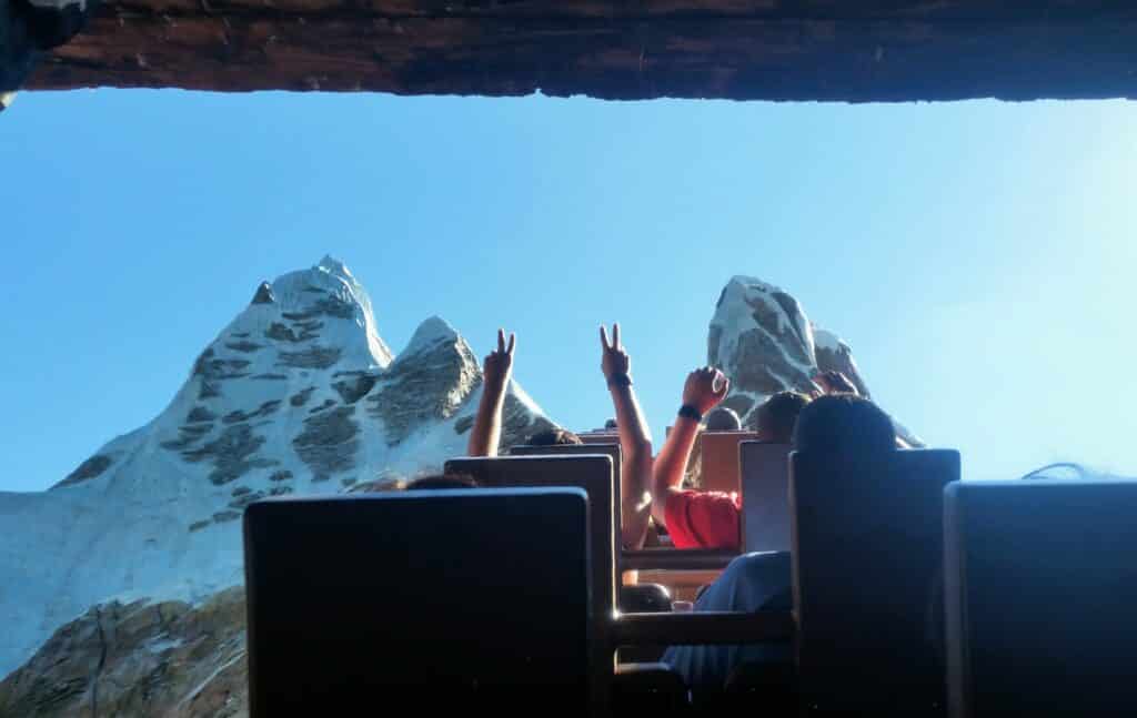 People on rollercoaster ride at Disney world scream and hold up hands at the top of Everest in Orlando